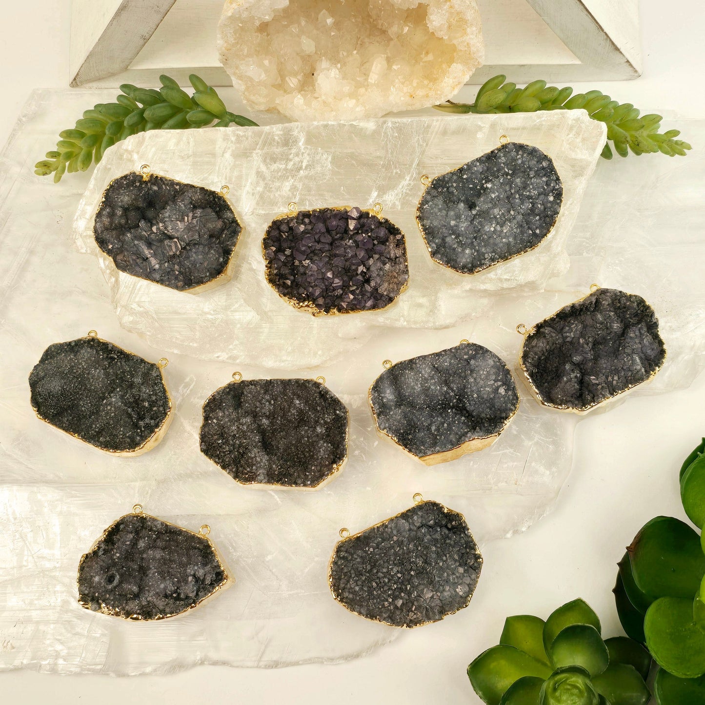 Gray Amethyst Druzy Oval Slab Pendant with 24k Gold Electroplated Edge and Double Bail nine on selenite platters with plants and props in the background