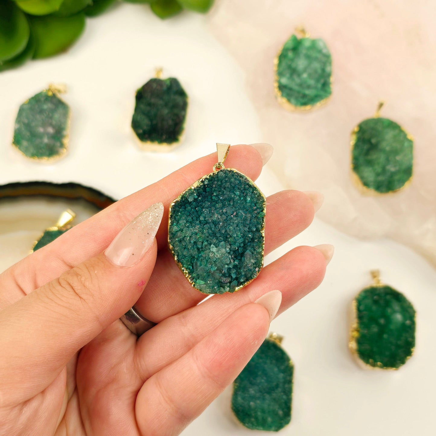 Green Druzy Freeform Pendant with 24k Gold Electroplated Edge and Bail one in hand for size reference with others in the background with props and plants