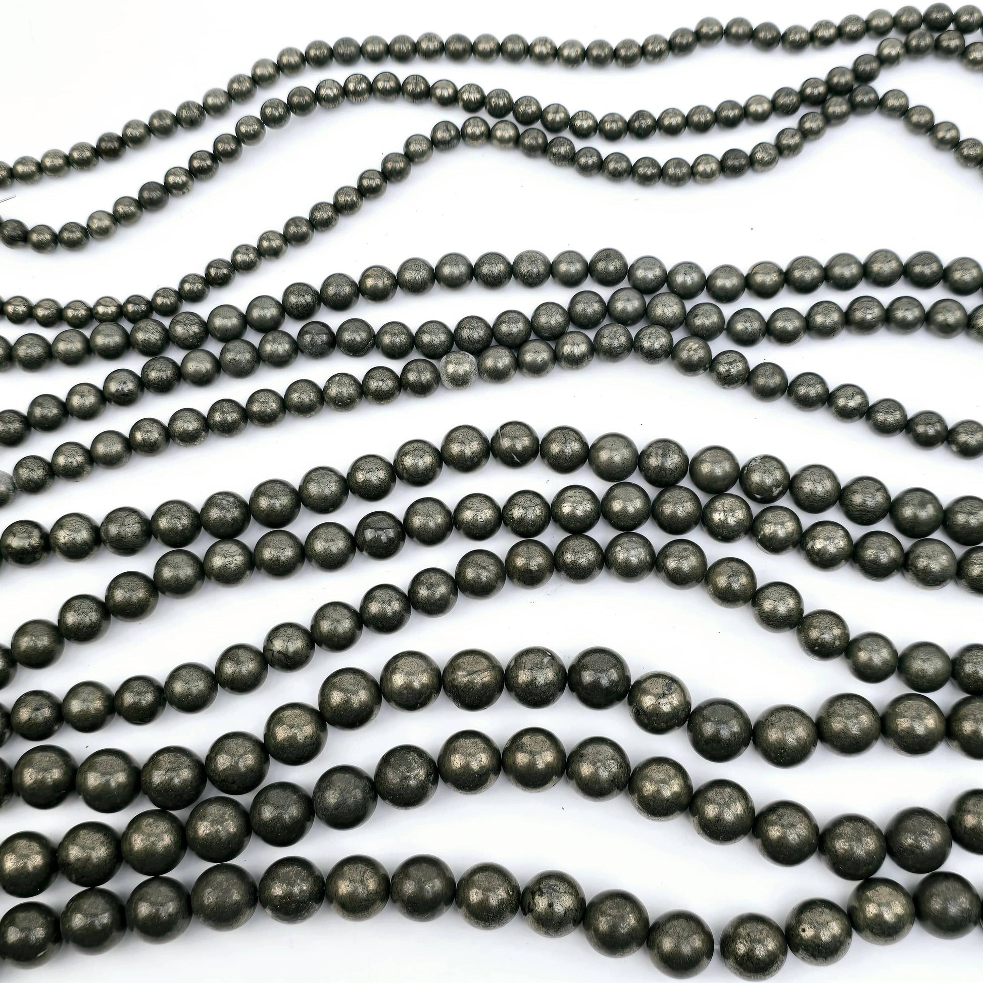 Pyrite Round Drilled Beads - 15.5" Strand - You Choose Size all sizes three of each strand lying horizontally on white surface