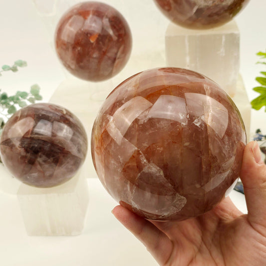 Guava Quartz Polished Crystal Sphere - By Weight - 2 kg to 3 kg weight variant in hand for size reference with other variants in the background with props and plants