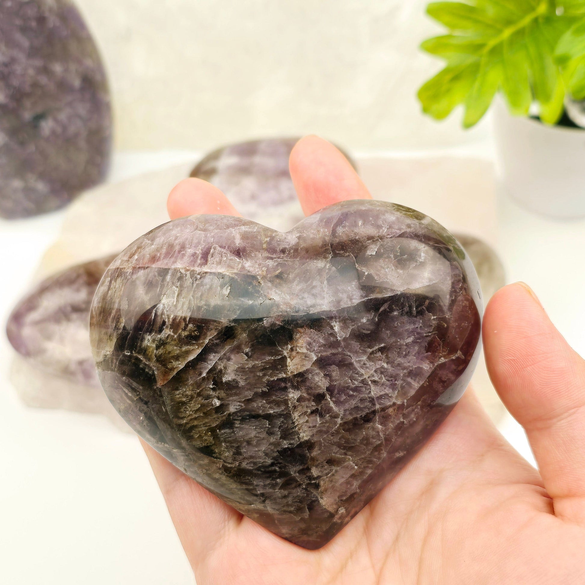 Amethyst Super Seven Polished Crystal Heart YOU CHOOSE - one in hand for size reference with others in background with props and plants