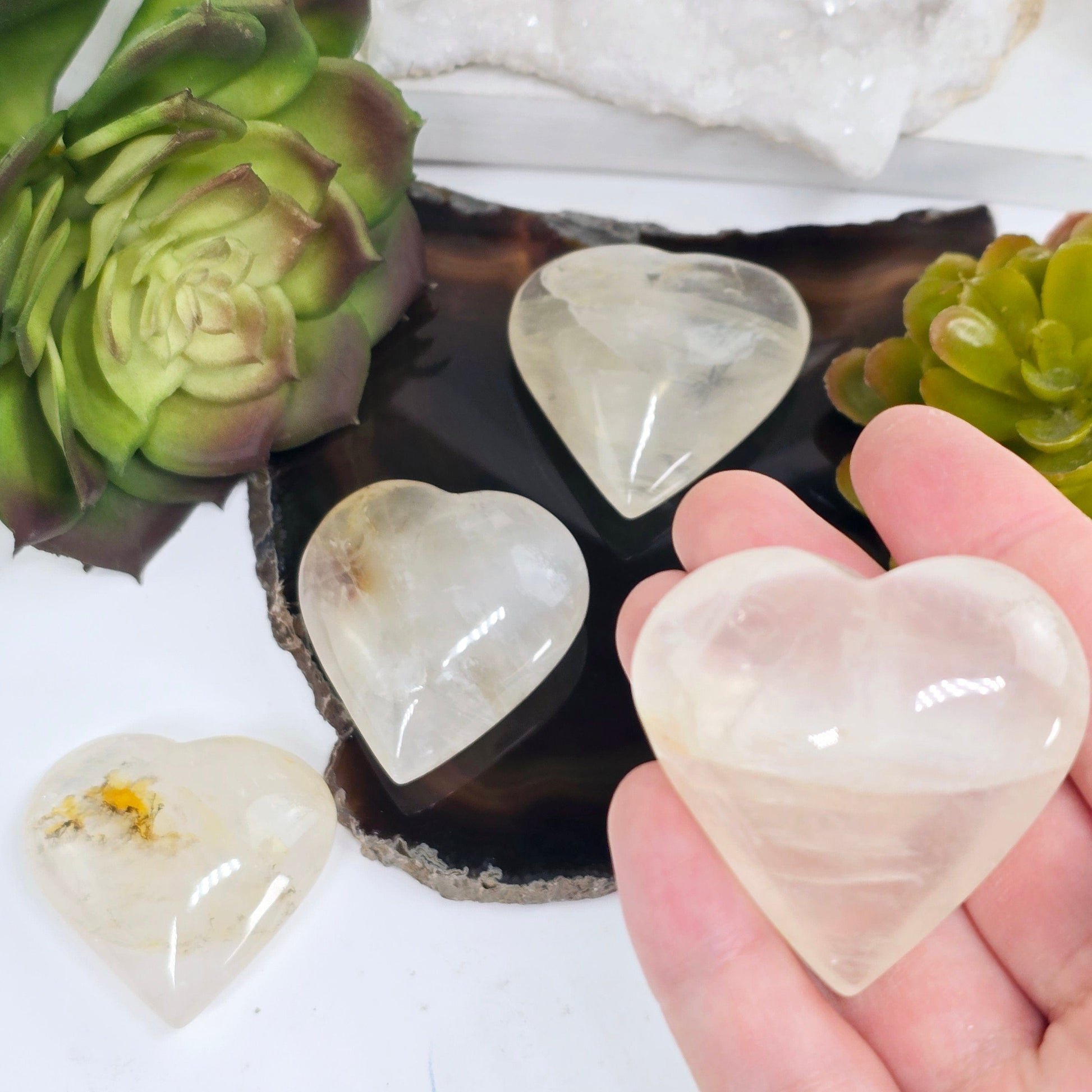 Golden Healer Small Polished Crystal Heart - You Choose #1 variant 3 in hand for size reference with others in background with props and plants