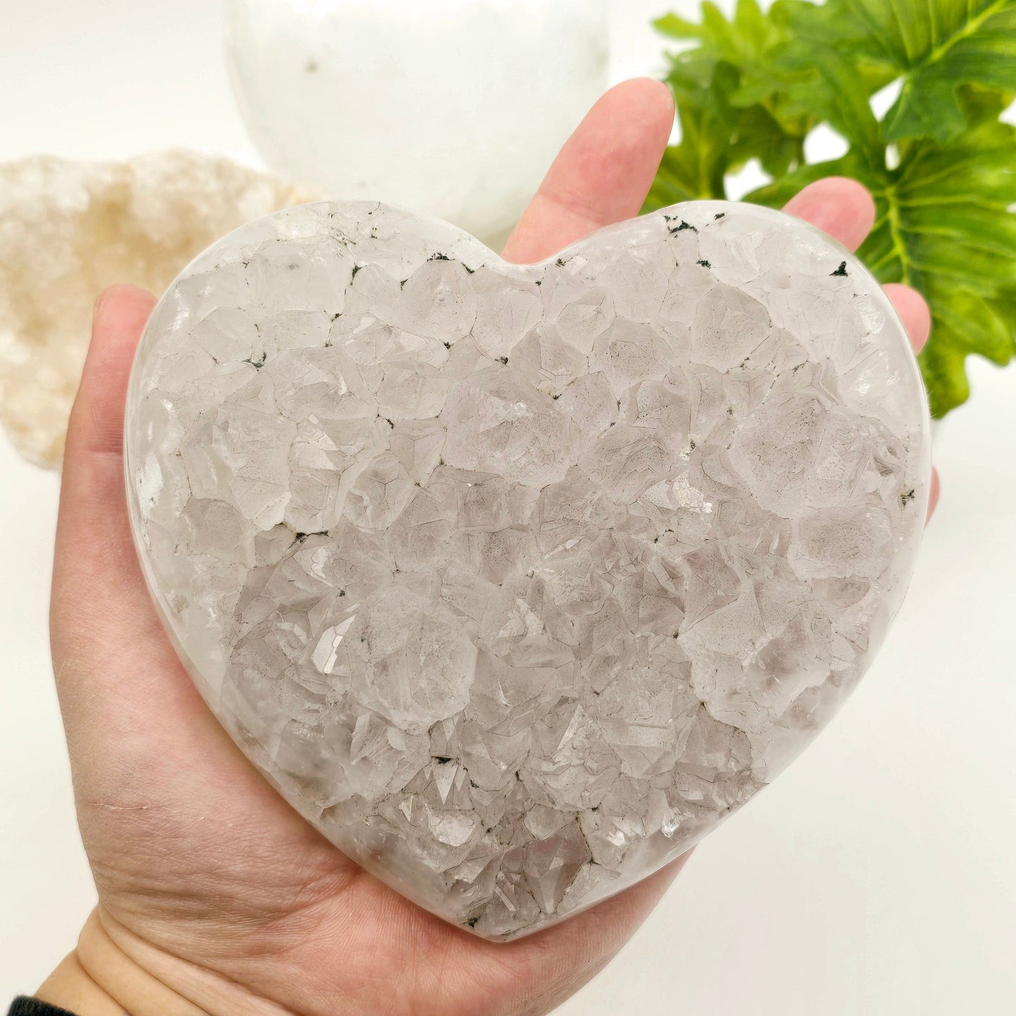 Light Amethyst Crystal Heart One-of-a-Kind in hand for size reference with props and plants in the background