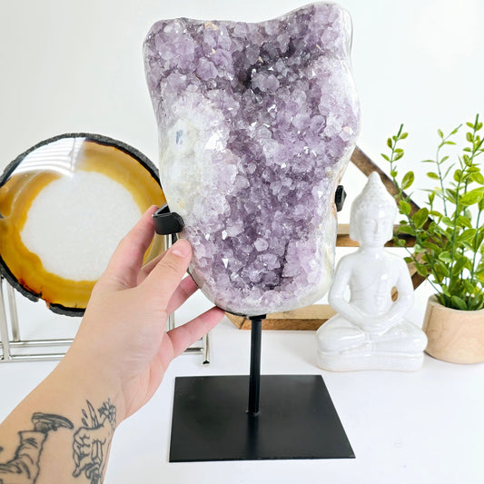 Amethyst - Large Crystal Cluster on Metal Stand #2 with hand for size reference with props and plants in hte background