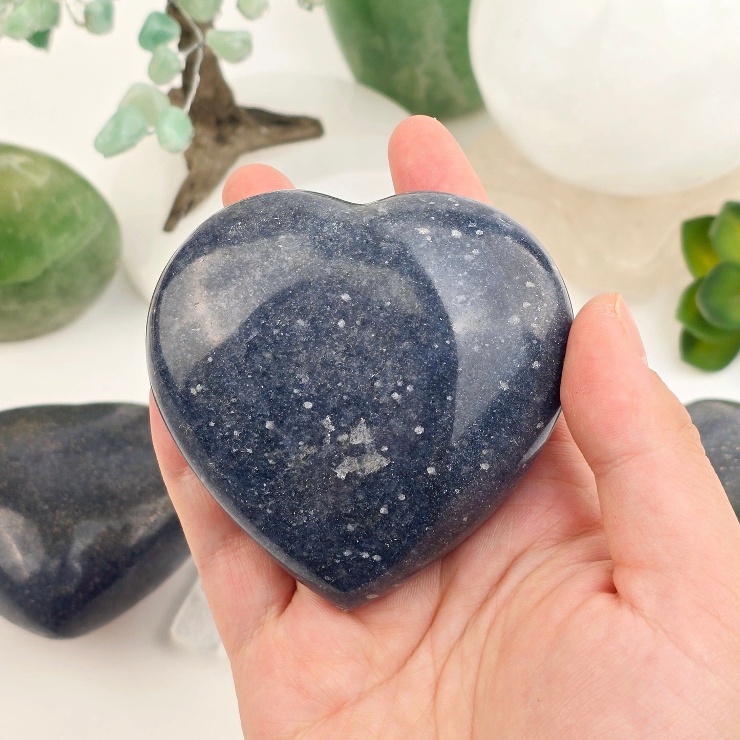 Lazulite Crystal Heart - You Choose - variant 1 in hand for size reference with others in background with props and plants in the background