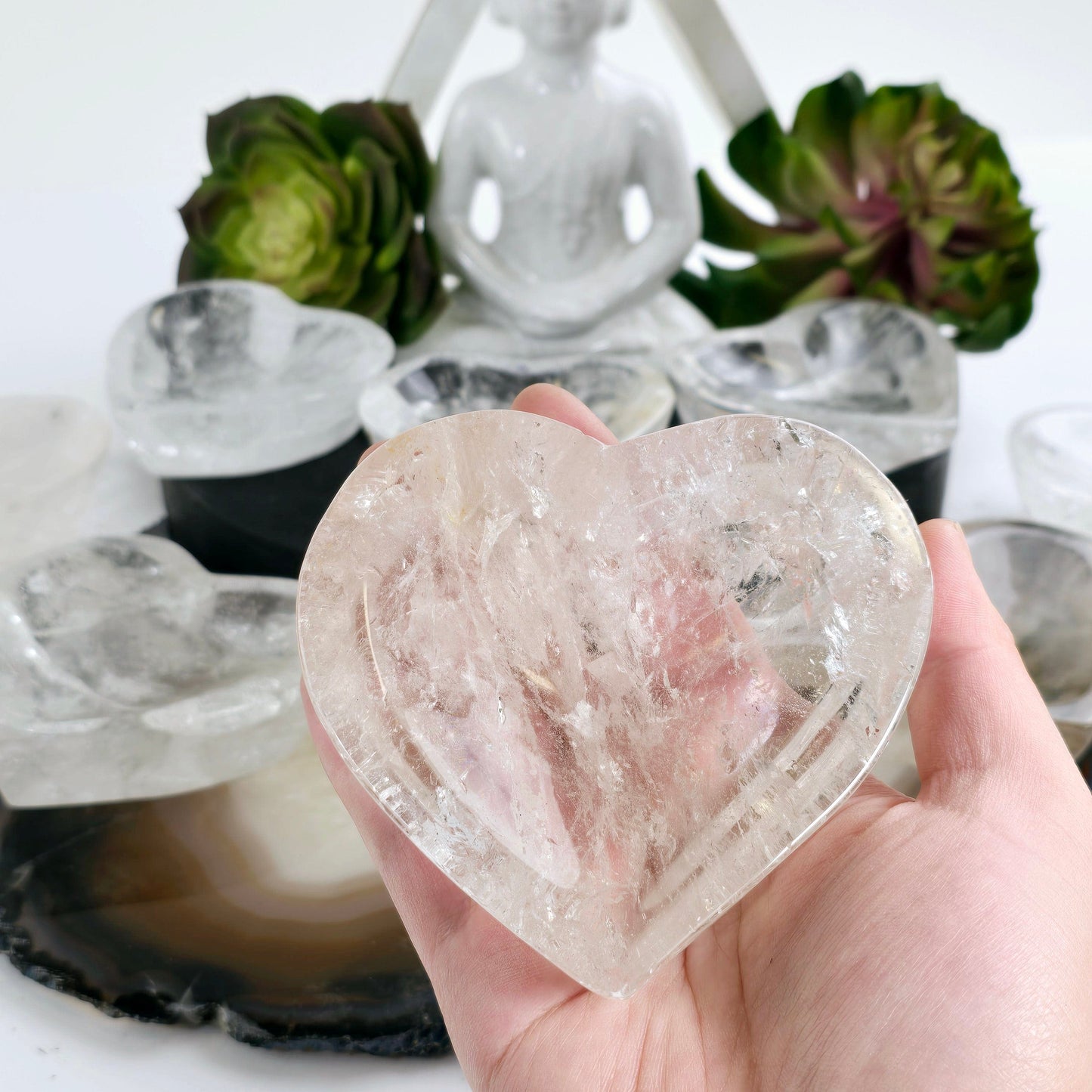 Crystal Quartz Heart Dish - You Choose #1 one in hand for size reference with others in the background with props and plants