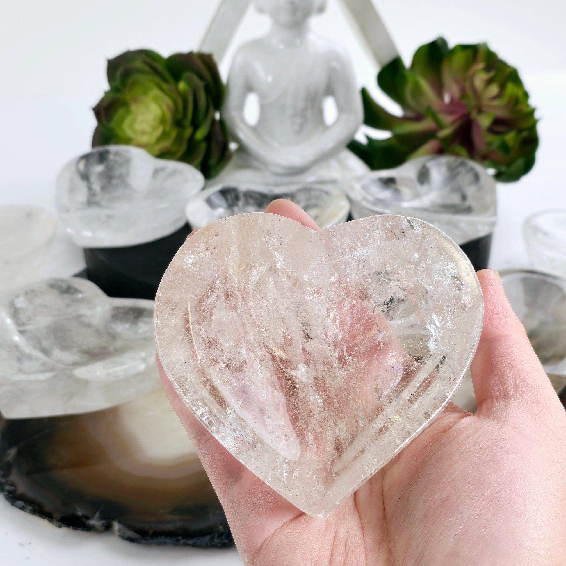 Crystal Quartz Heart Dish - You Choose #1 one in hand for size reference with others in the background with props and plants