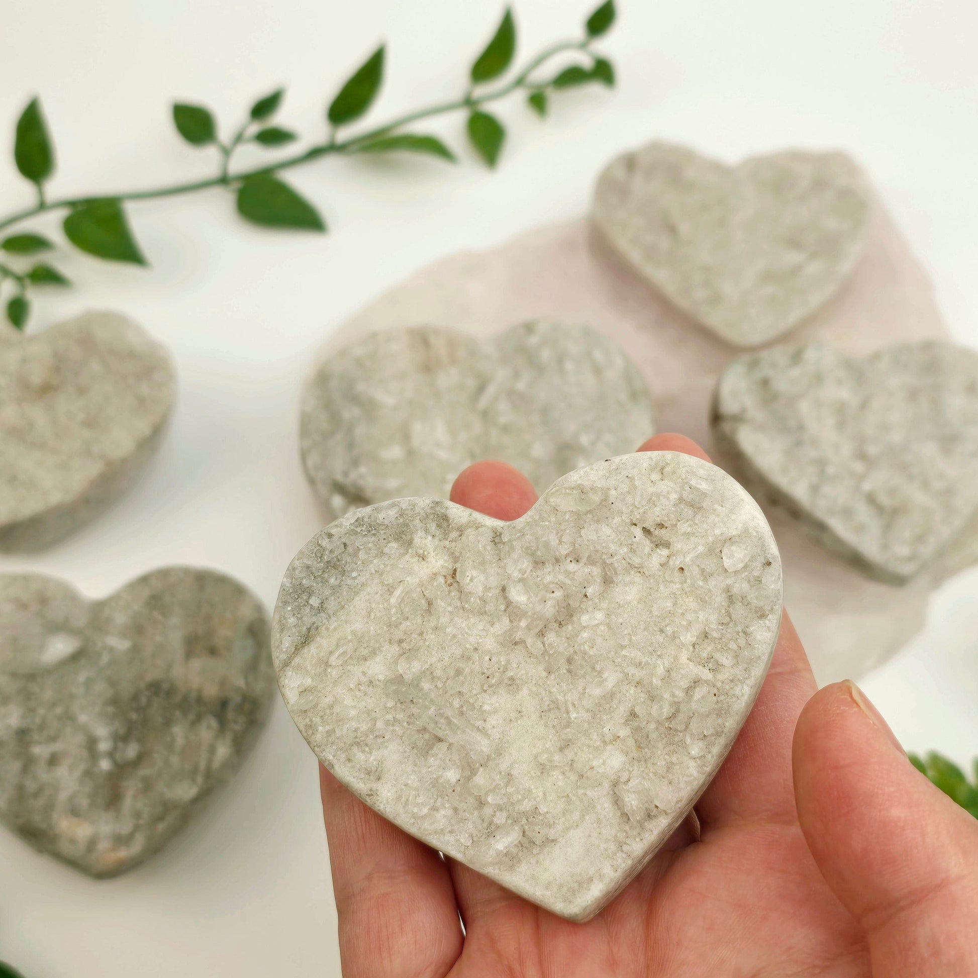 Crystal Quartz Cluster Polished Heart - You Choose #1 - one in hand for size reference with others in the background with props and plants
