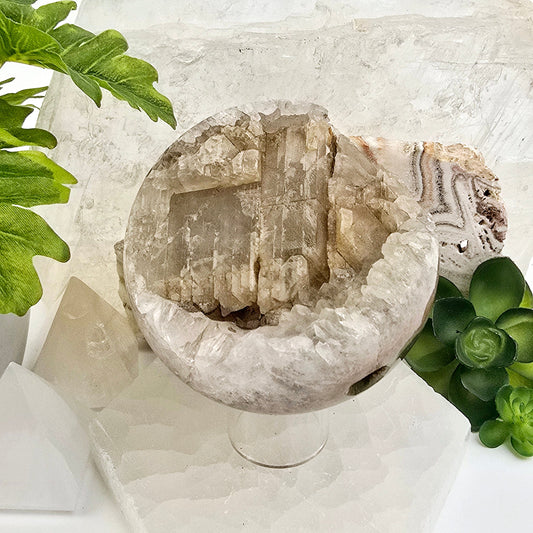 Crystal Quartz Cluster with Calcite Sphere - One-of-a-Kind on sphere stand with props and plants in the background front view