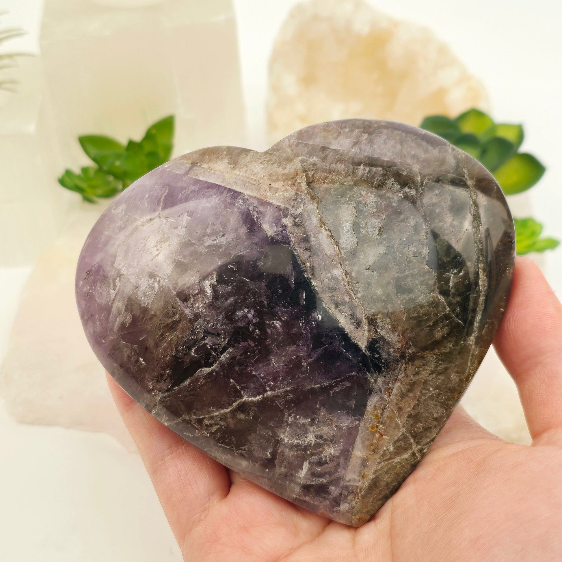 Super Seven Polished Crystal Heart - One-of-a-Kind #1 in hand for size reference with plants and props in the background