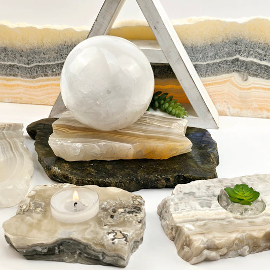 Grey Travertine Calcite - Grey Onyx - Crystal Candle Holder - By Size one large one with a white sphere and two small ones with a candle and succulent with props and plants in the background
