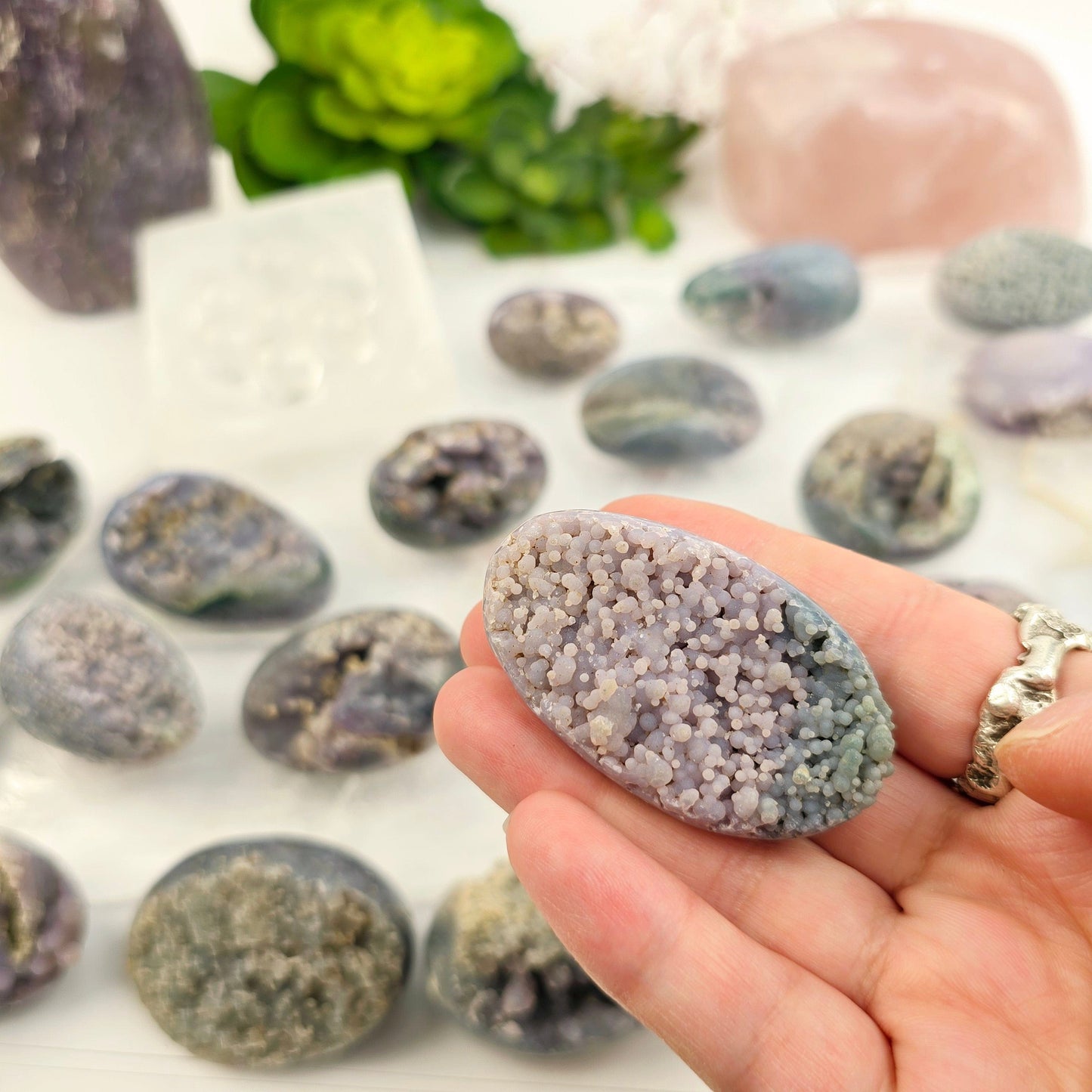 Grape Agate Polished Crystal Egg from Indonesia - You Choose #1 one variant in hand with other variants in the background with props and plants