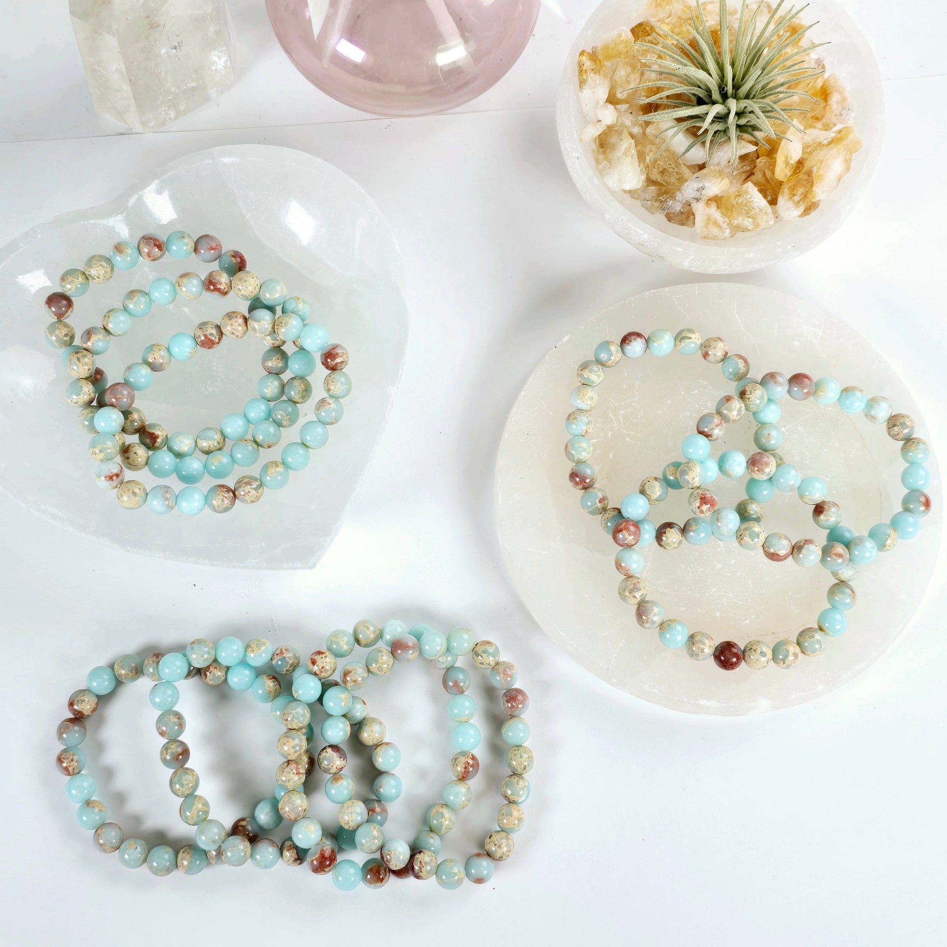 Imperial Jasper Crystal Bracelet - 8mm Beaded Bracelet ten arranged in aesthetic manner in crystal dish, white coaster, and white surface with props and plants