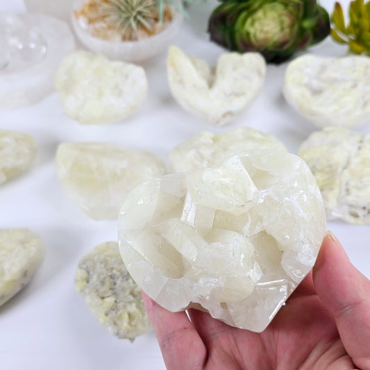 Sulfur Quartz Polished Crystal Cluster Heart - You Choose #2 variant 7 in hand for size reference with others in the background with props and plants