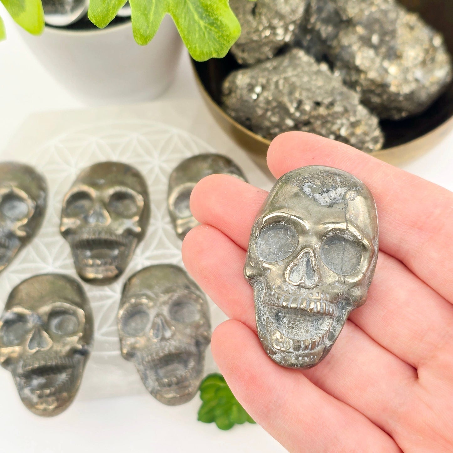 Pyrite Crystal Skull Cabochon - You Choose variant 1 in hand for size reference with other variants in the background with props and plants