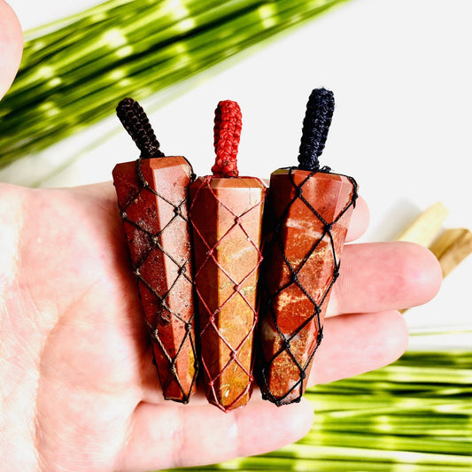 Hand holding up 3 Red Jasper Points - Netted Pendants with plants blurred on white background
