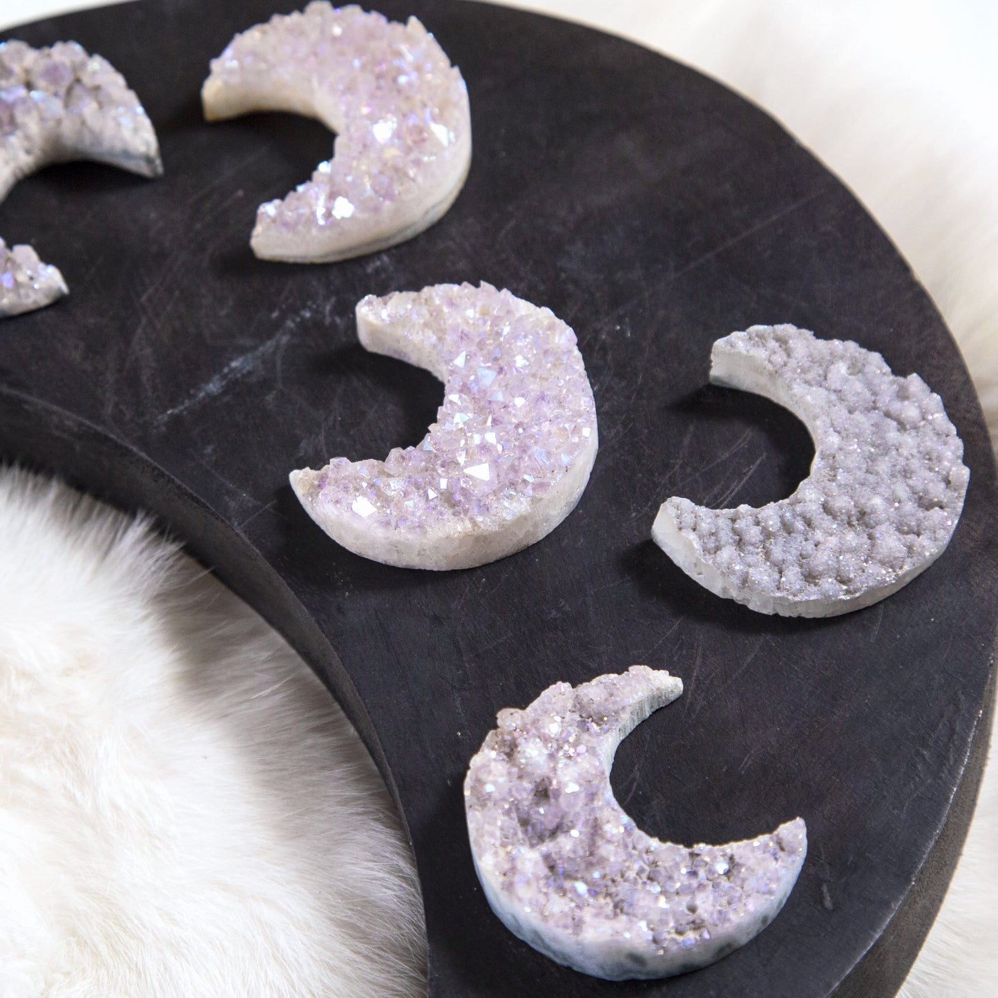 up close shot of moon shaped titanium druzy pendants on wooden moon shaped platter