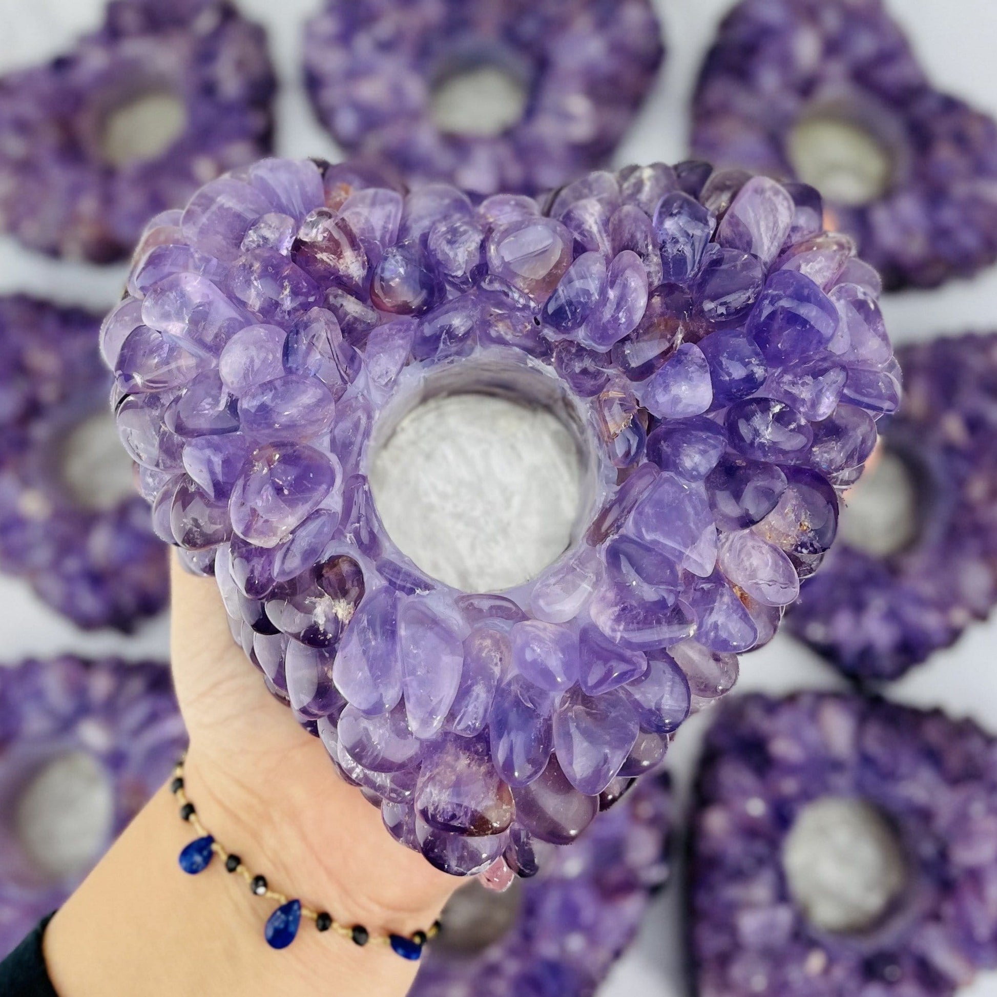 hand holding up amethyst tumbled heart stone candle holder with others blurred in the background