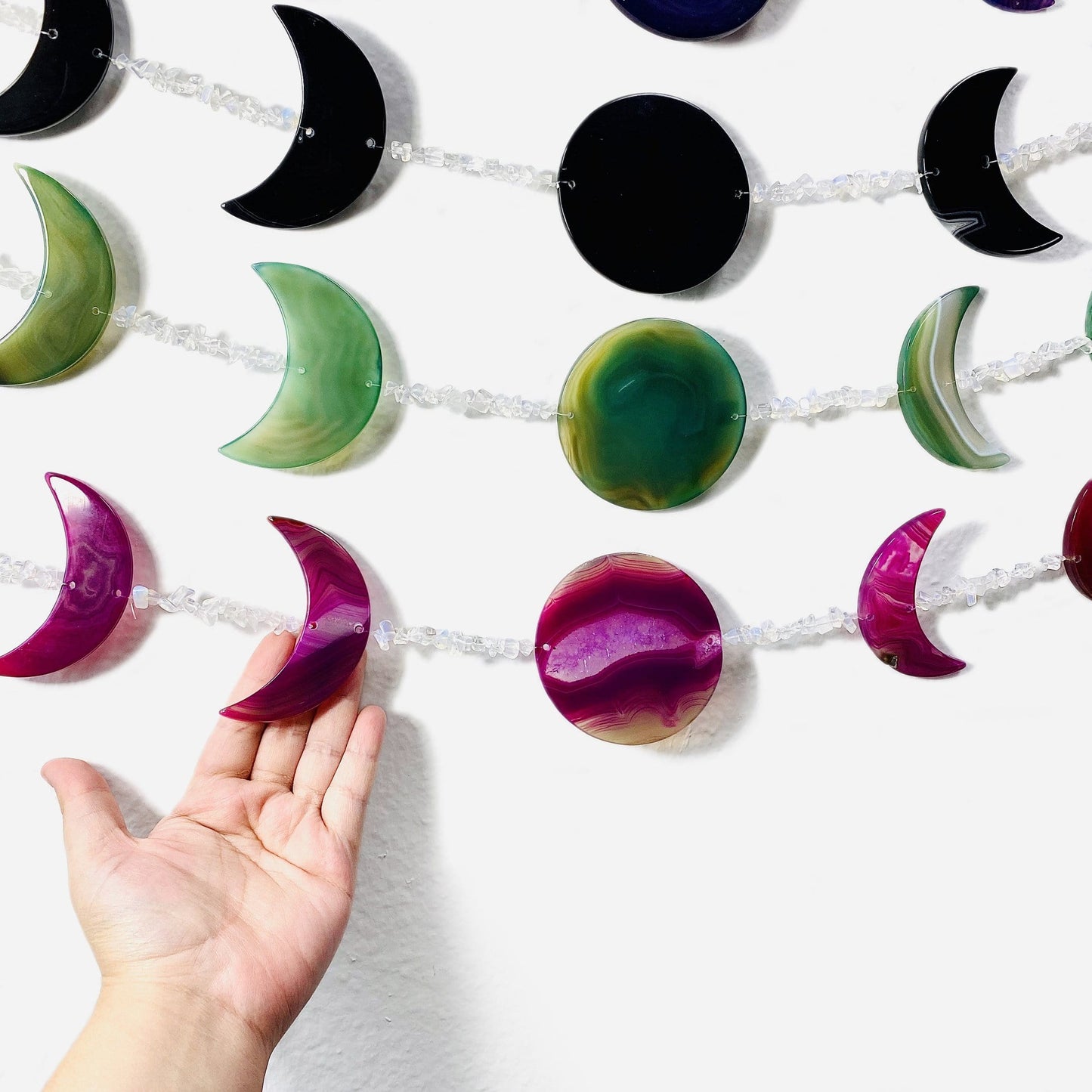 Another close up image of wall hangings on a white background with a hand touching one