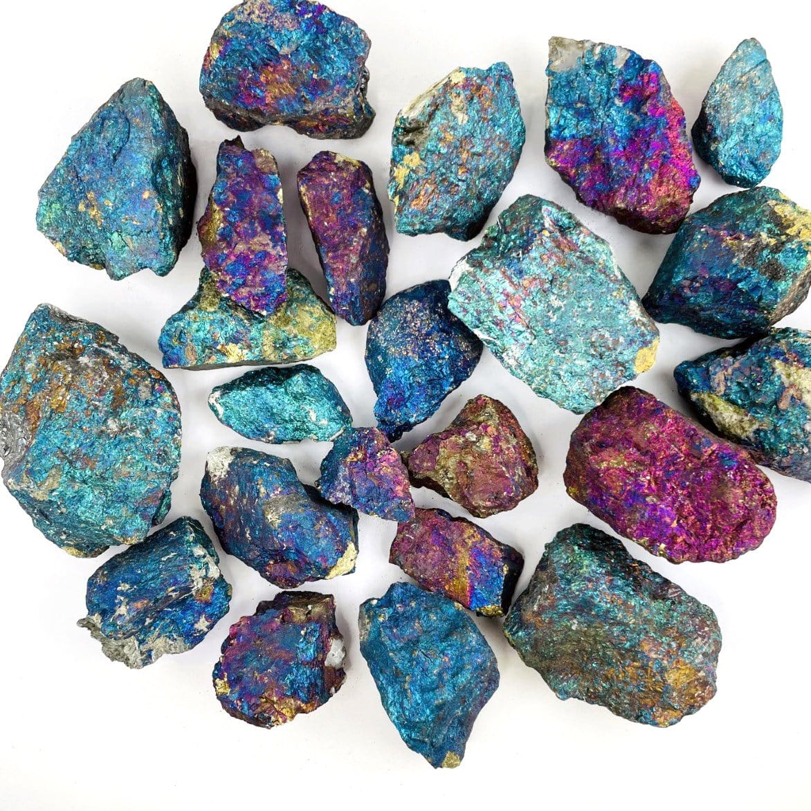 Assorted sizes of peacock ore rough stones on a white background.  They are a metallic shade of pinks, blues, and purples.