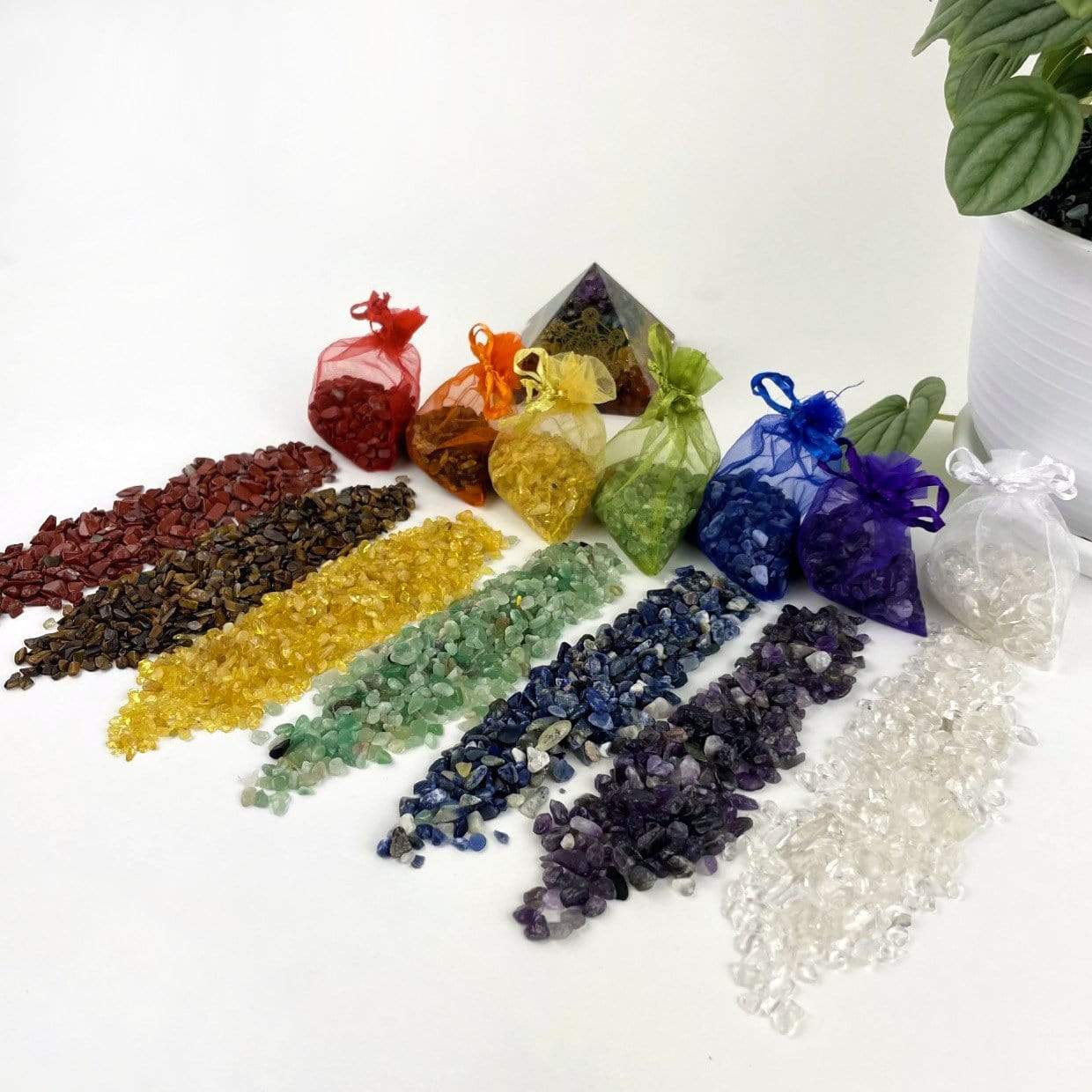 Red Jasper, Tiger Eye, Citrine, Green Quartz, Amethyst, and Crystal Quartz small chips laid out next to their bags. Each bag matches the color of the stone and is see through mesh.  Jasper is red, Tiger eye is brown but has an orange bag.  Citrine is yellow , Green quartz is green, Sodalite is blue, Amethyst is purple and crystal quartz is white.