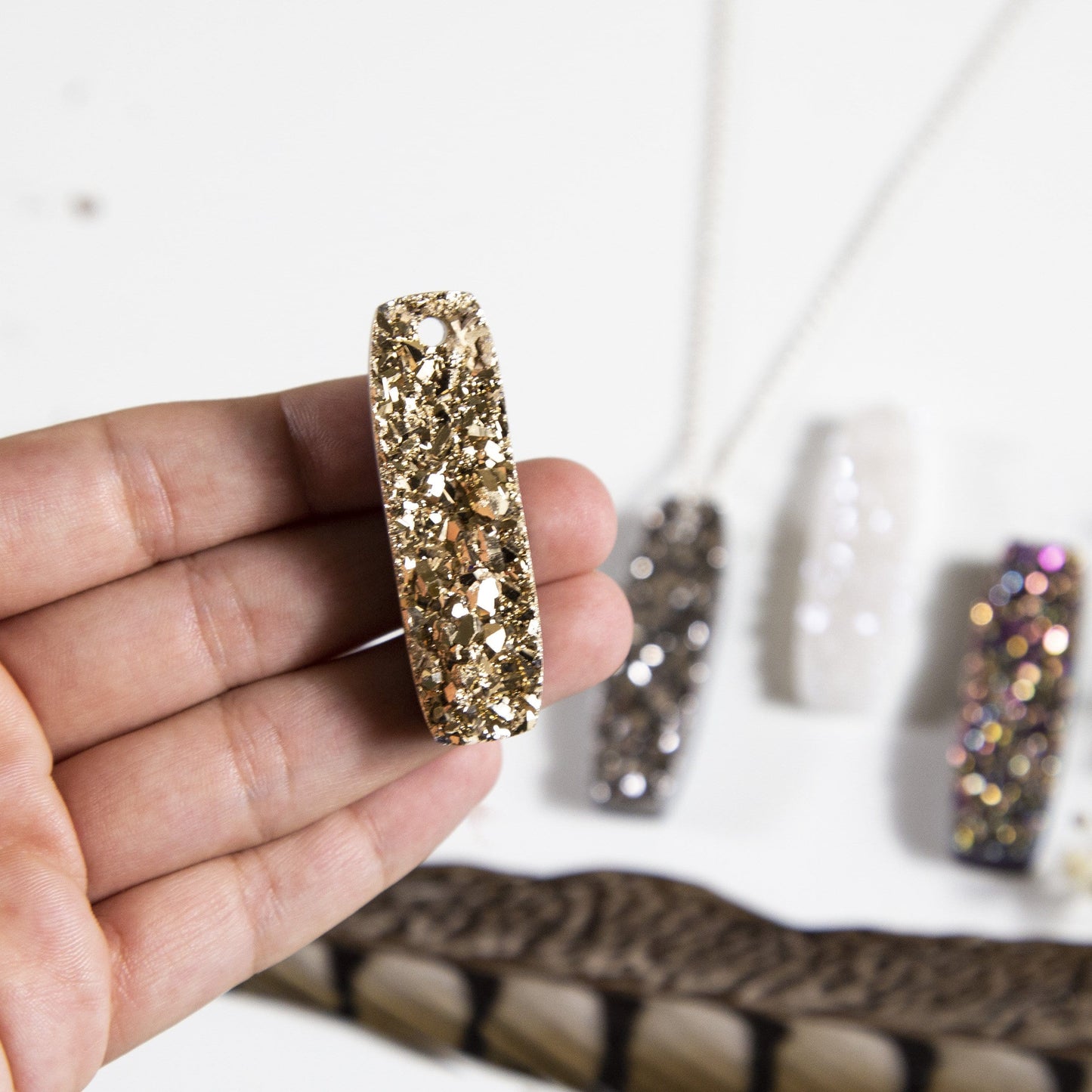 hand holding up druzy bar drilled with decorations in the background