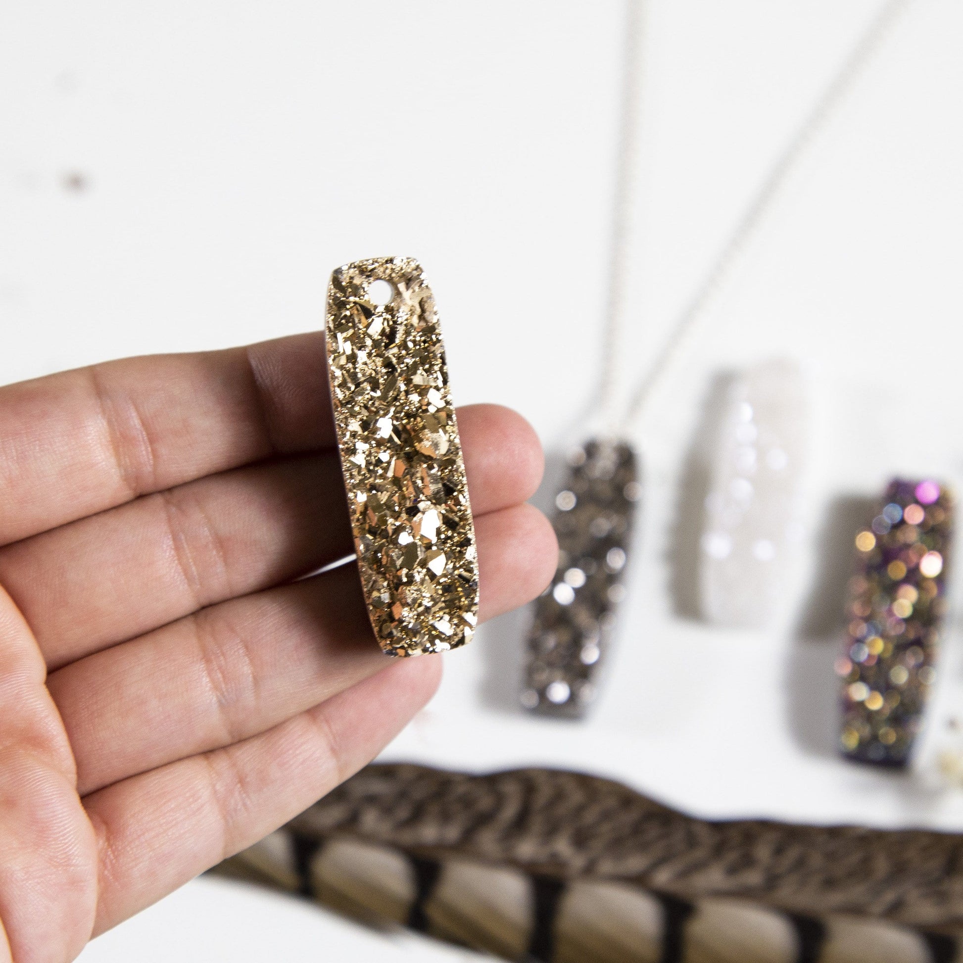 hand holding up druzy bar drilled with decorations in the background