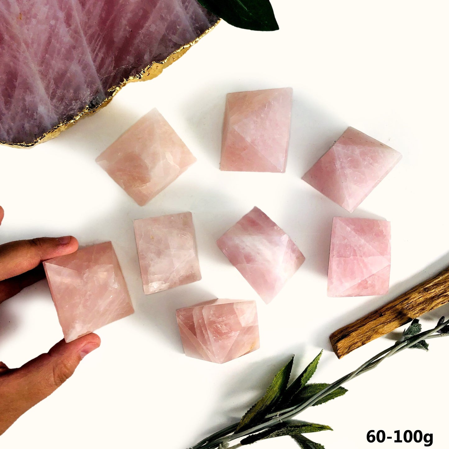 Hand holding 60-100g Rose Quartz Diamond Shaped Stone with others scattered on white background with decorations