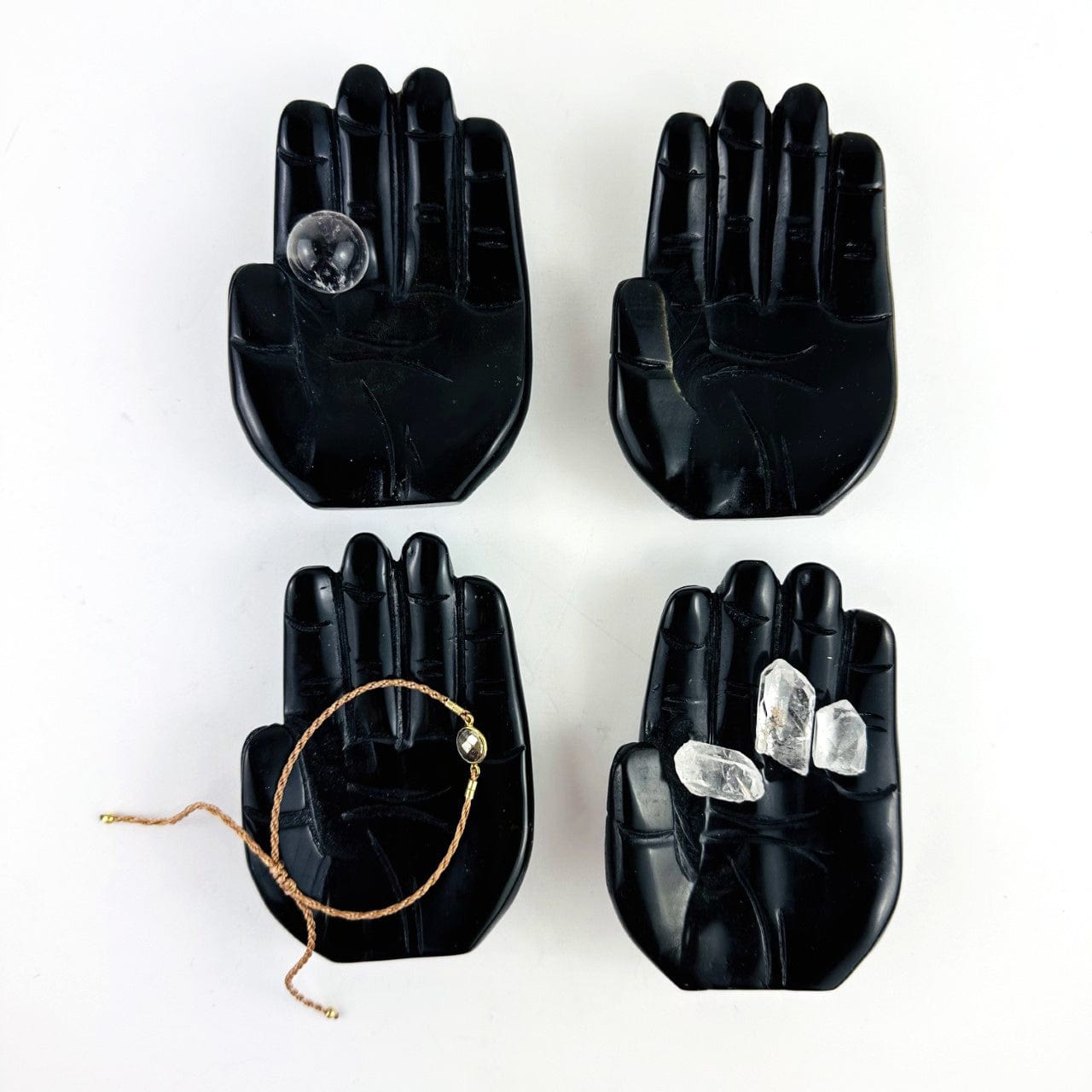 Hamsa Hand Stone Carvings in black obsidian, shown with crystals in one, a small sphere in one and a bracelet in one