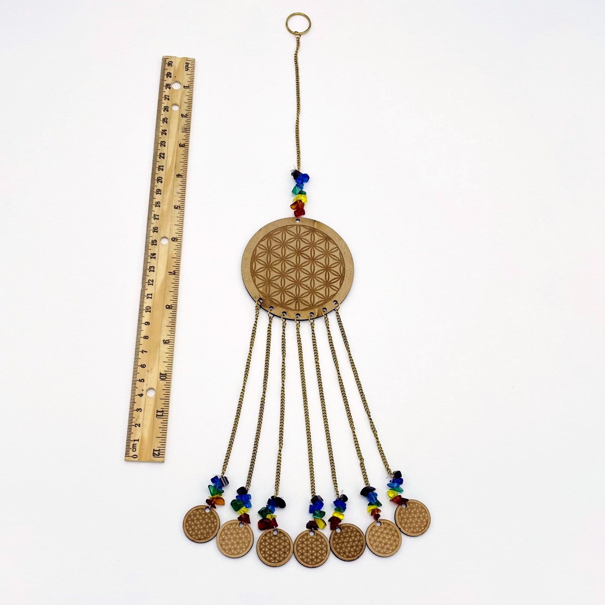 Engraved Wooden Flower of Life next to a ruler on white background.