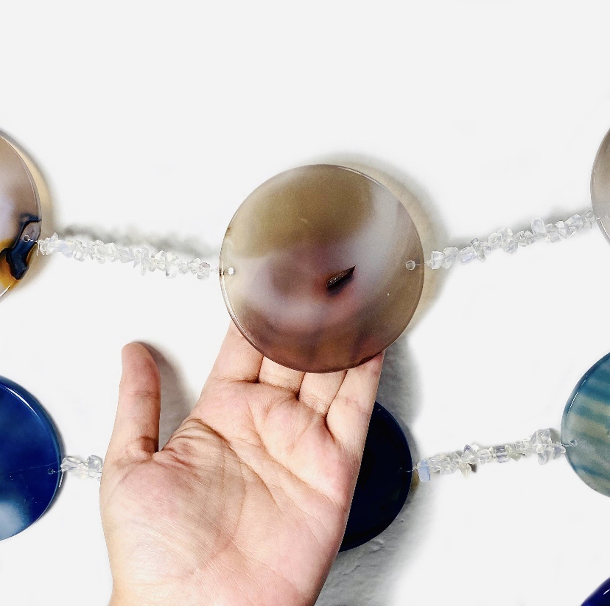 View of center round agate in the moon phase wall hanging on a white background with a hand touching the moon.  It is around 4 fingers wide