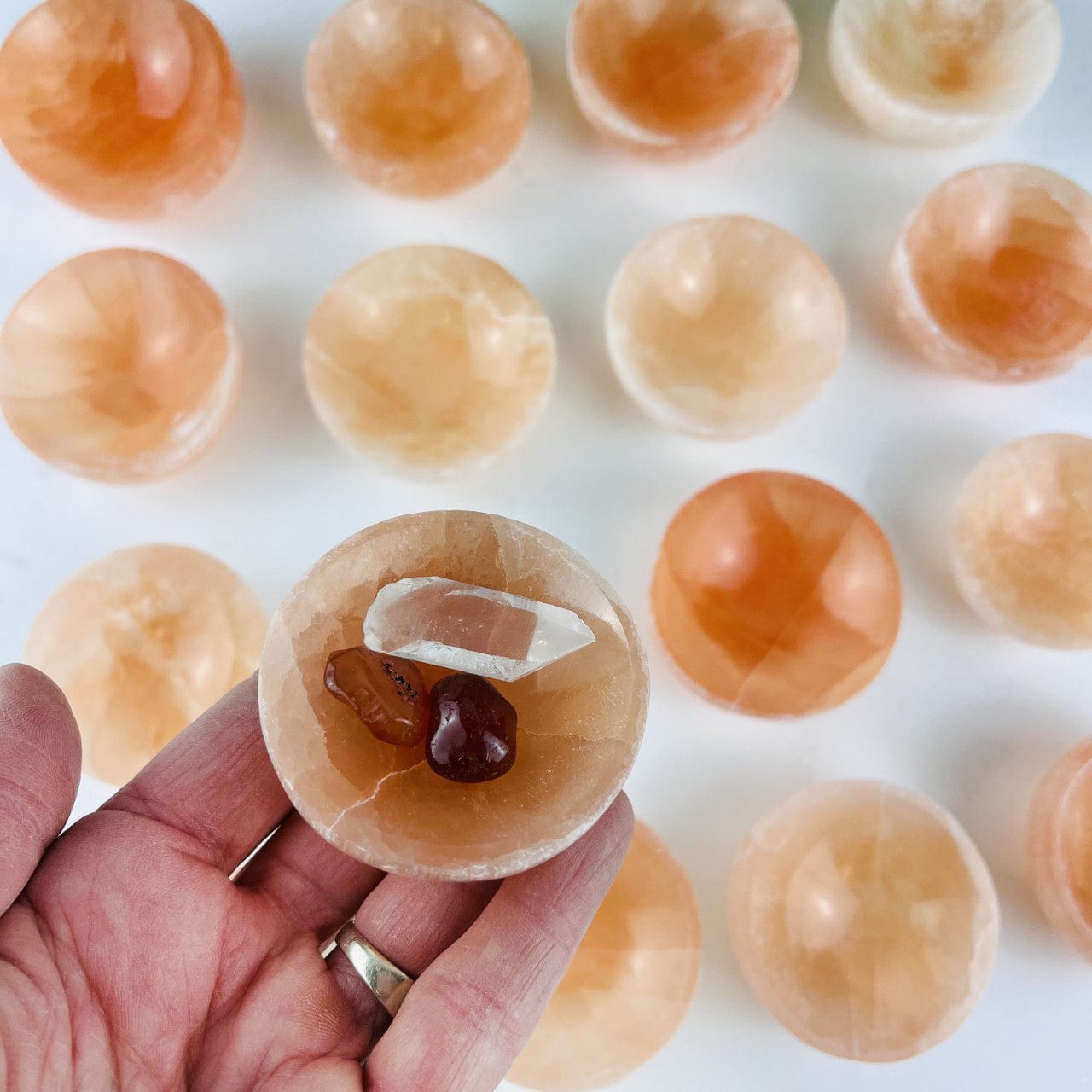 Orange Selenite Bowl- 6CM size in a hand for size reference, and others in the background showing various colors of this stone