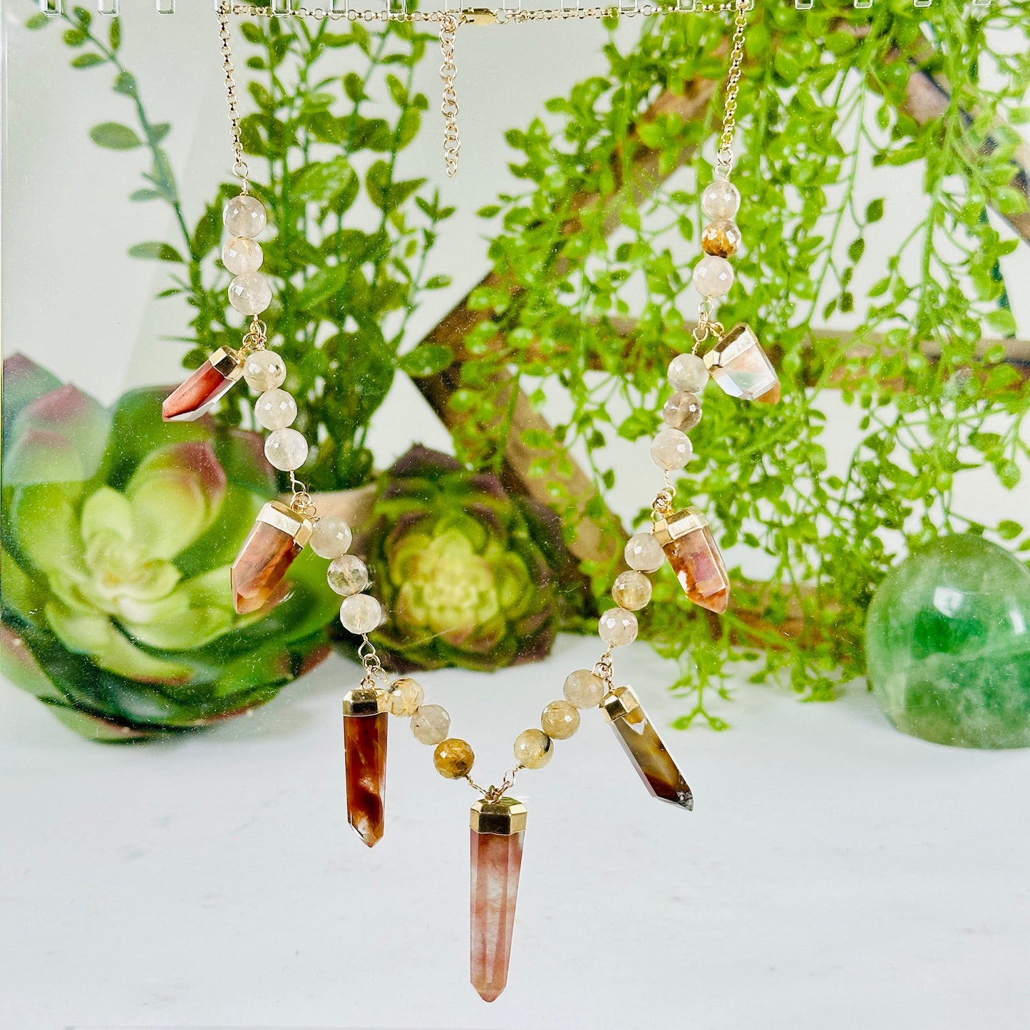 Amphibole and Rutilated Quartz Crystal Charm Necklace - Gold over Sterling Silver with plants and props in the background