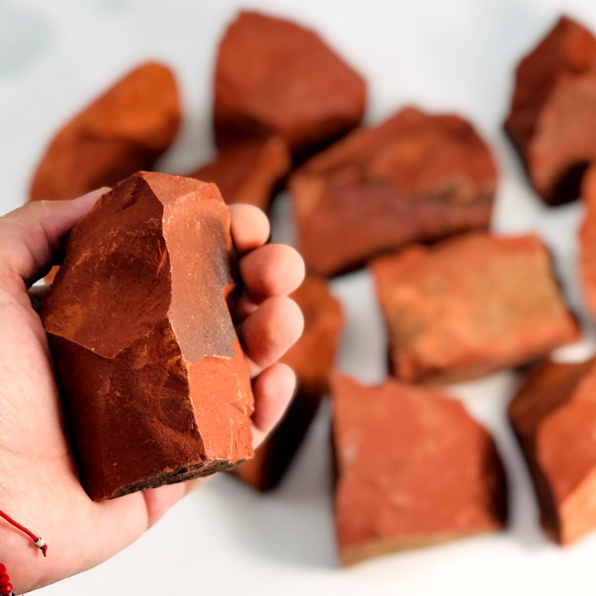 Hand holding up Red Jasper Rough Stone with others blurred in the background