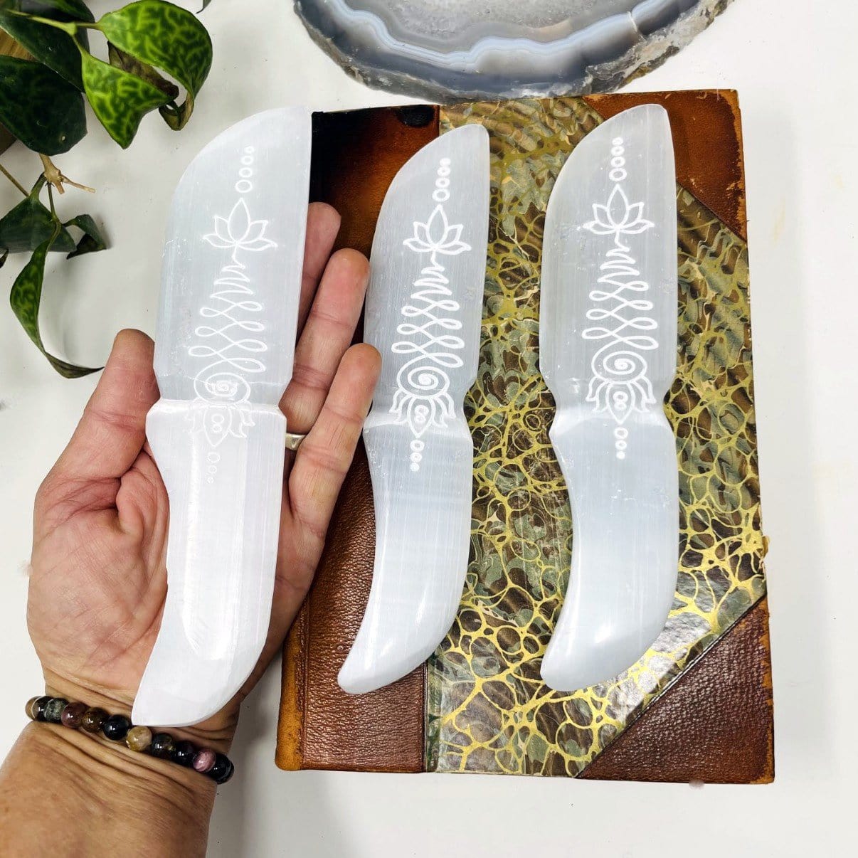 selenite knife with unalome engraving in hand for size reference with others on display for possible variations and engraving details