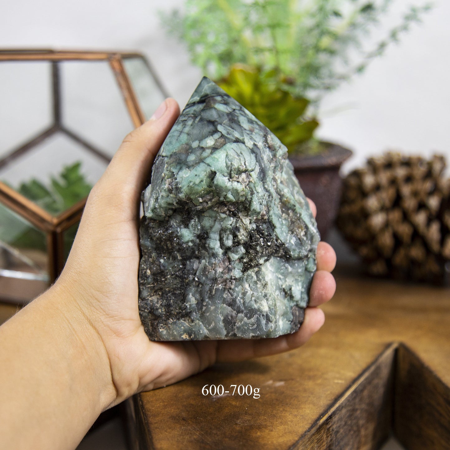 Semi Polished point Emerald Stone in hand showing the weight of 600 to 700g on white background