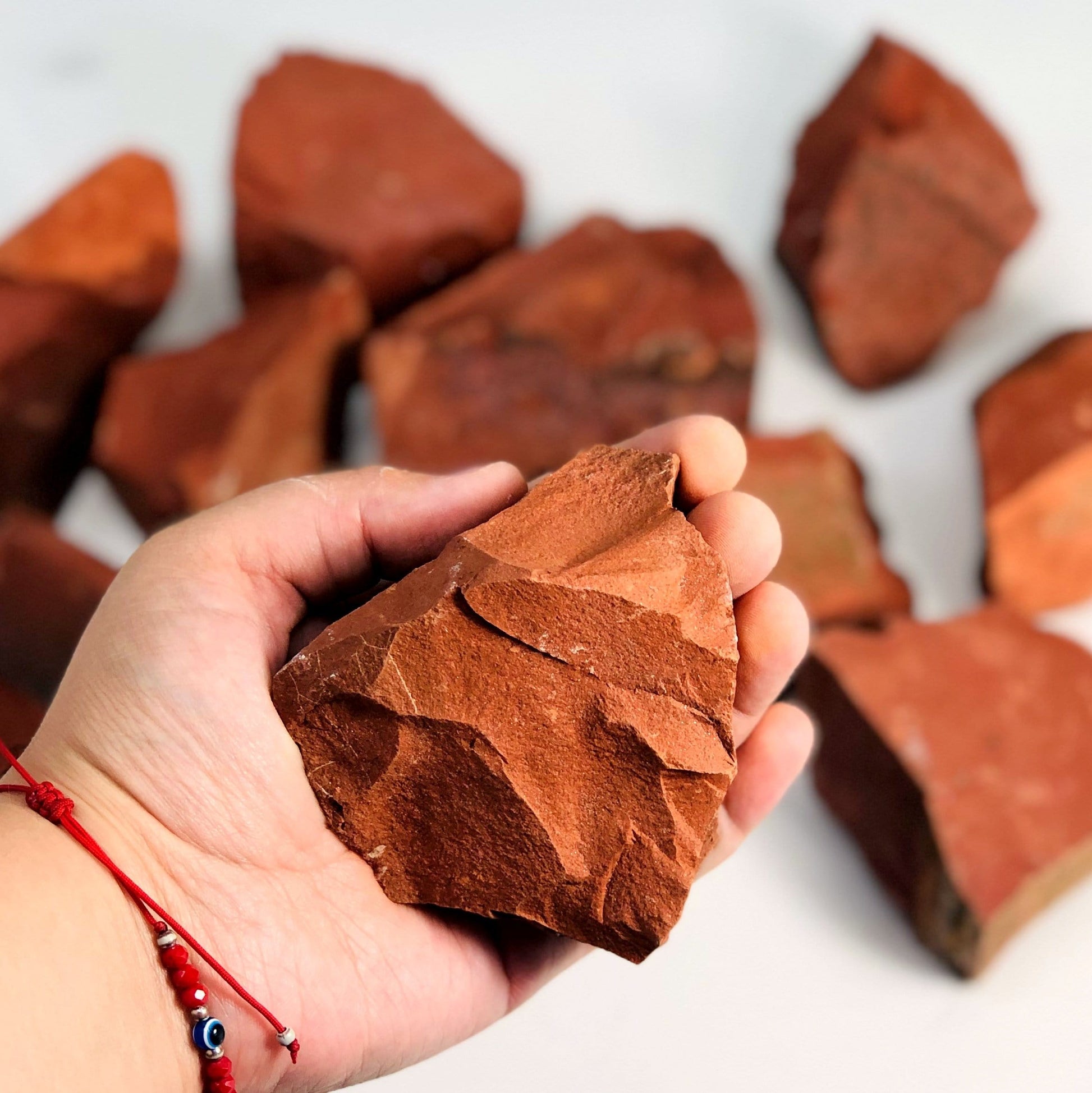 Hand holding up Red Jasper Rough Stone with others blurred on white background