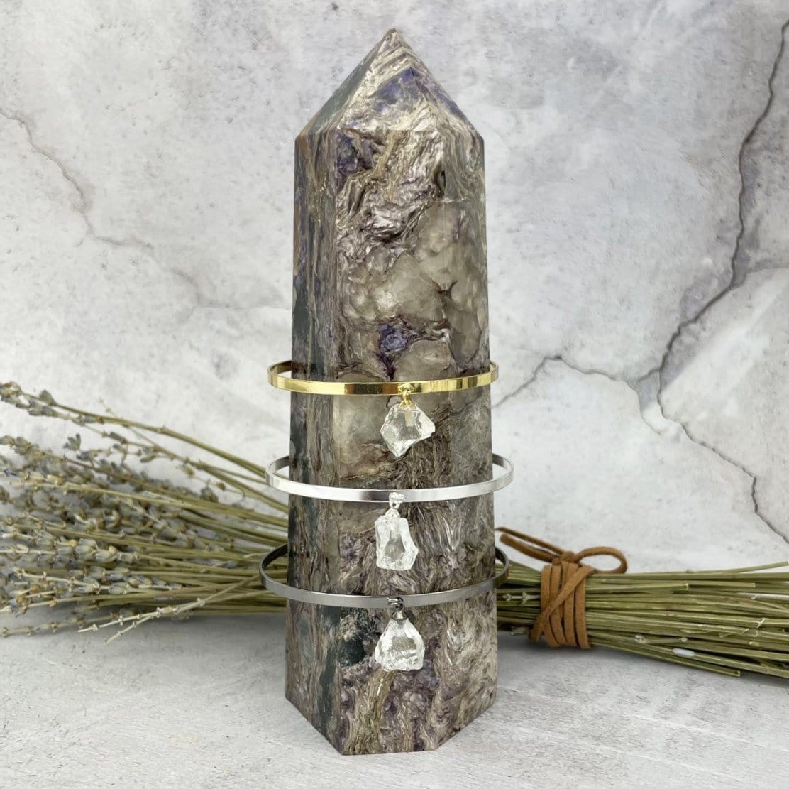 Gold and silver bracelets that are thin metal with a rough crystal quartz hanging from the middle.  Pictured here on a purple and white point.