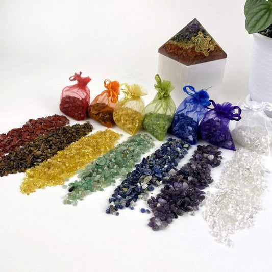 Red Jasper, Tiger Eye, Citrine, Green Quartz, Amethyst, and Crystal Quartz small chips laid out next to their bags. Each bag matches the color of the stone and is see through mesh.  Jasper is red, Tiger eye is brown but has an orange bag.  Citrine is yellow , Green quartz is green, Sodalite is blue, Amethyst is purple and crystal quartz is white.