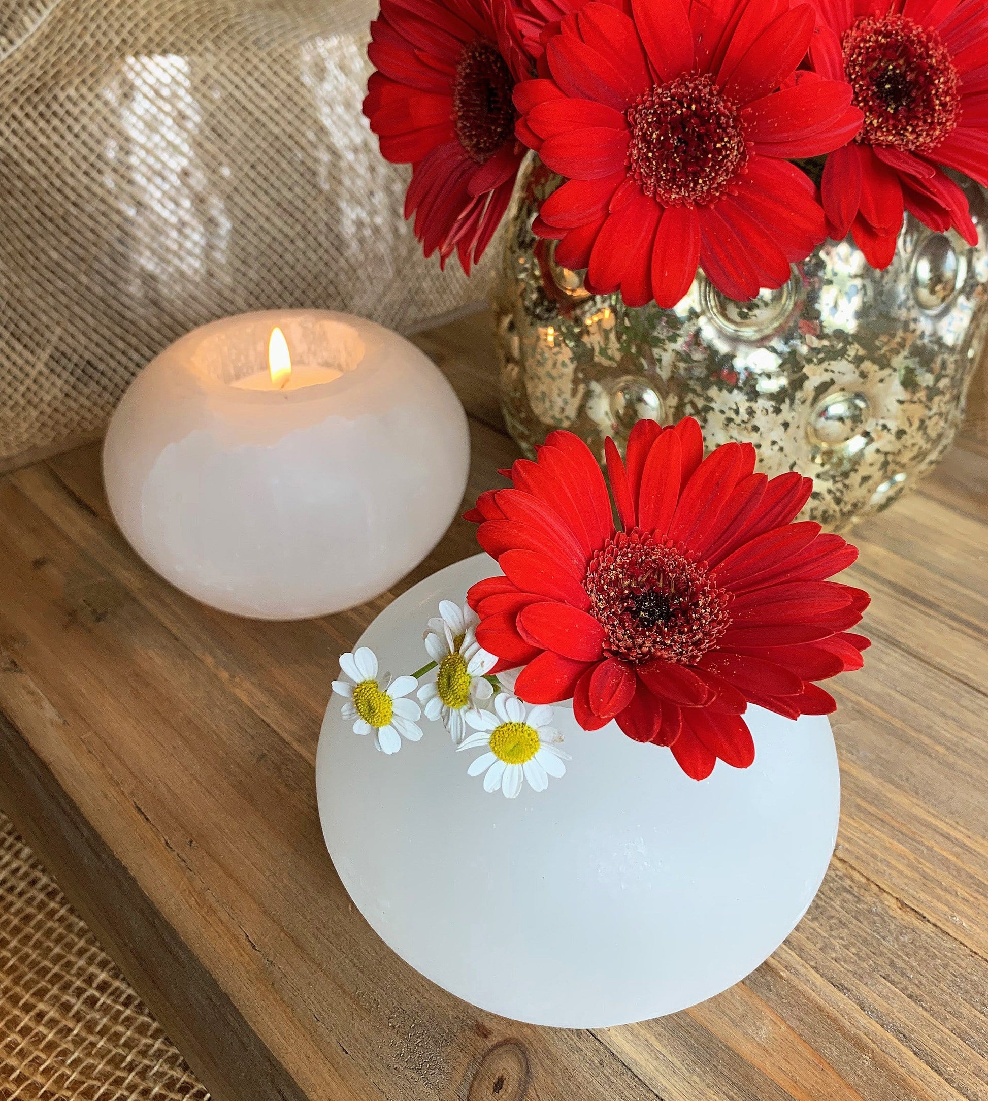 Selenite Sphere Candle Holders, one lit with a votive and the other holding a couple flowers 