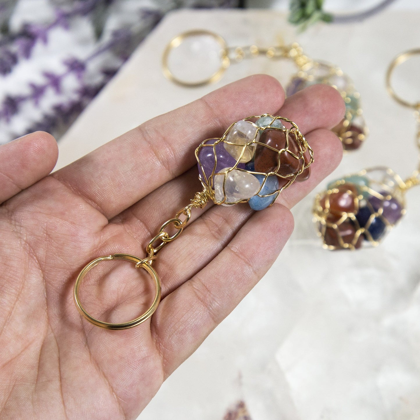 one seven stone chakra tumbled stone gold keychain in hand for size reference with others in background display