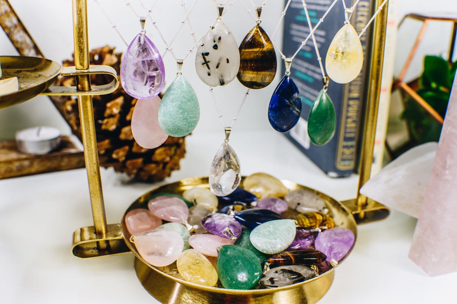 Gemstone Teardrop Pendants of various stones hanging from a holder and sitting in a tray, showing all the sshades and variations