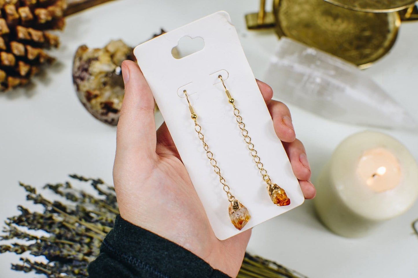 Cirtine point earring on a gold chain on a white card and held in a woman's hand.