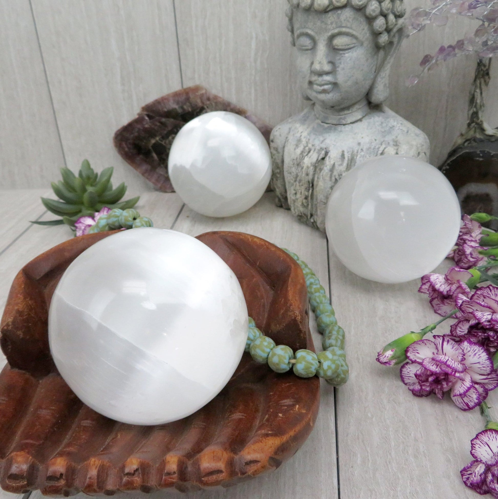 selenite sphere in wooden hand bowl with others in background display