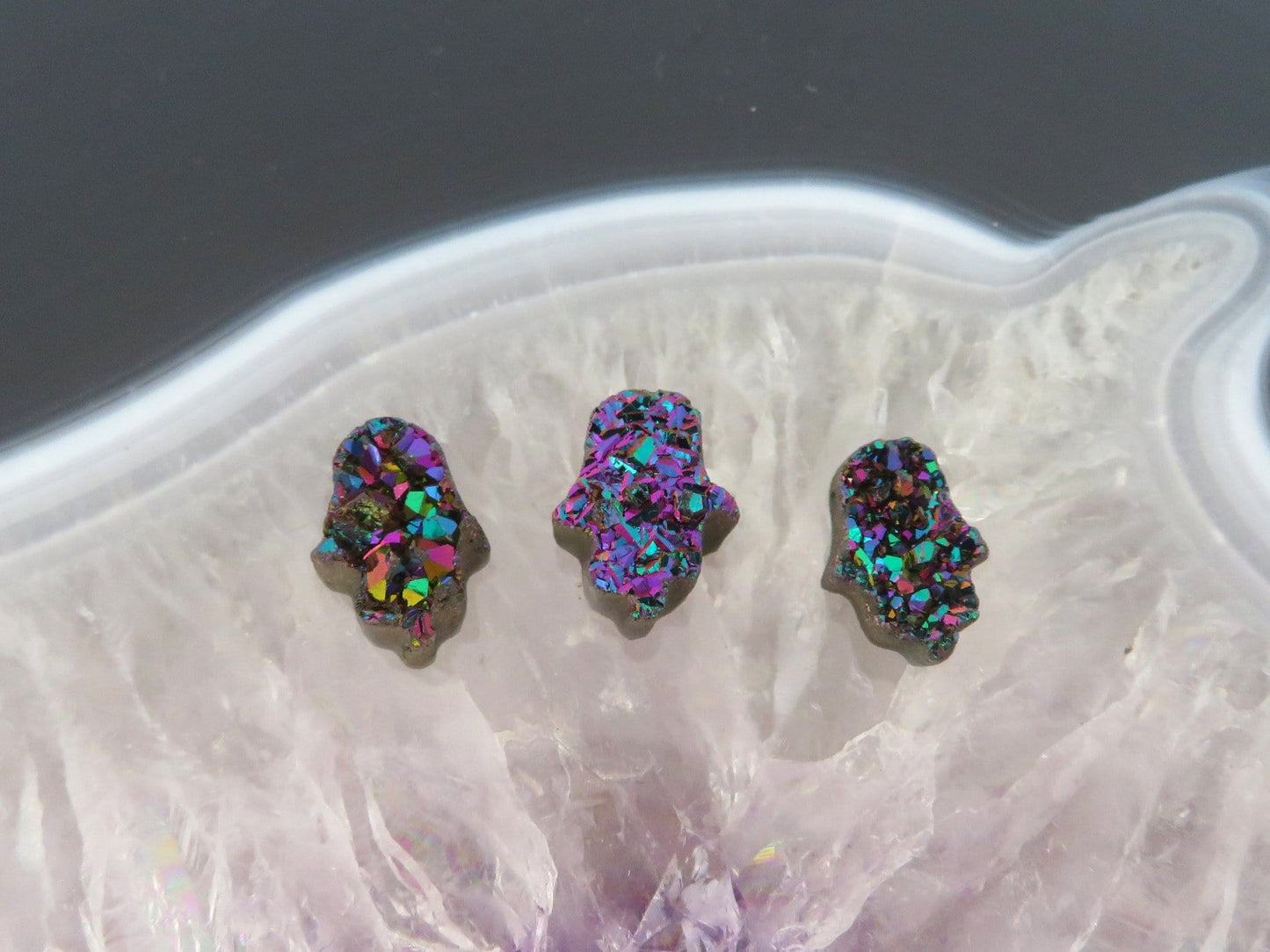 head drilled hamsa bead titanium druzy in assorted color shown against light backgrounds