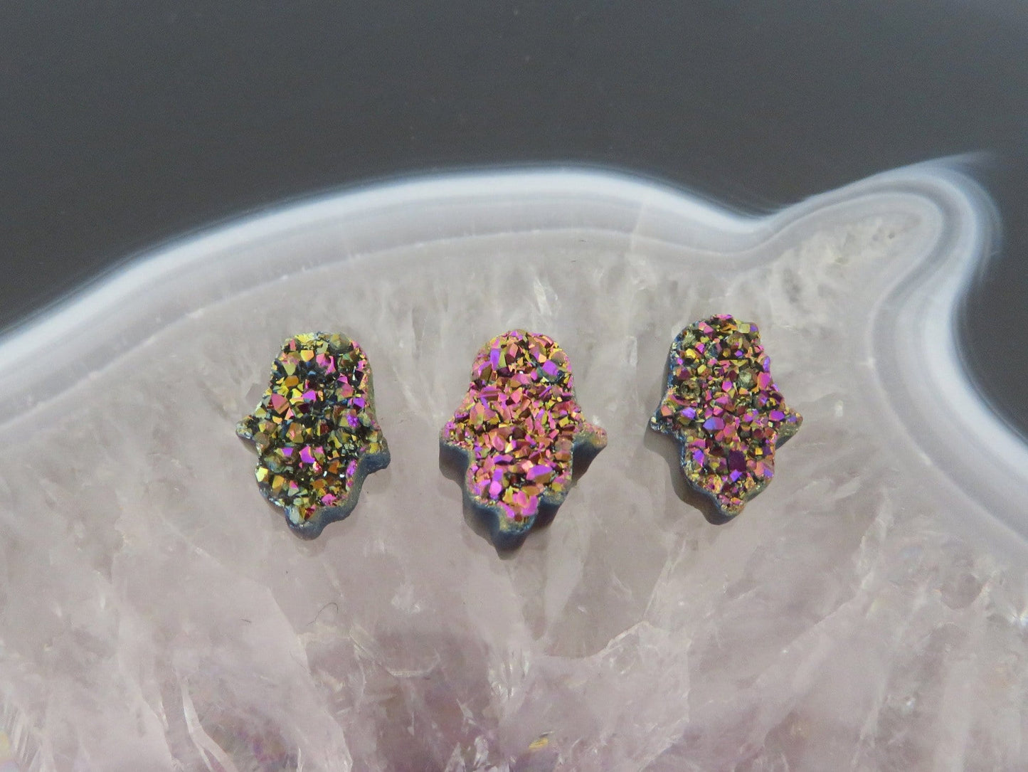 head drilled hamsa bead titanium druzy in assorted color shown against light backgrounds