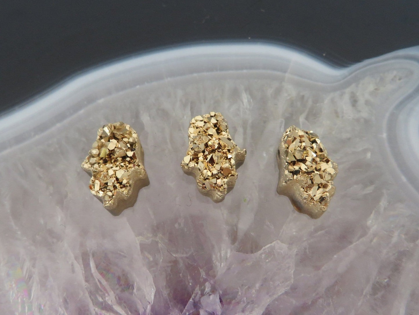 head drilled hamsa bead titanium druzy in assorted color shown against light backgrounds