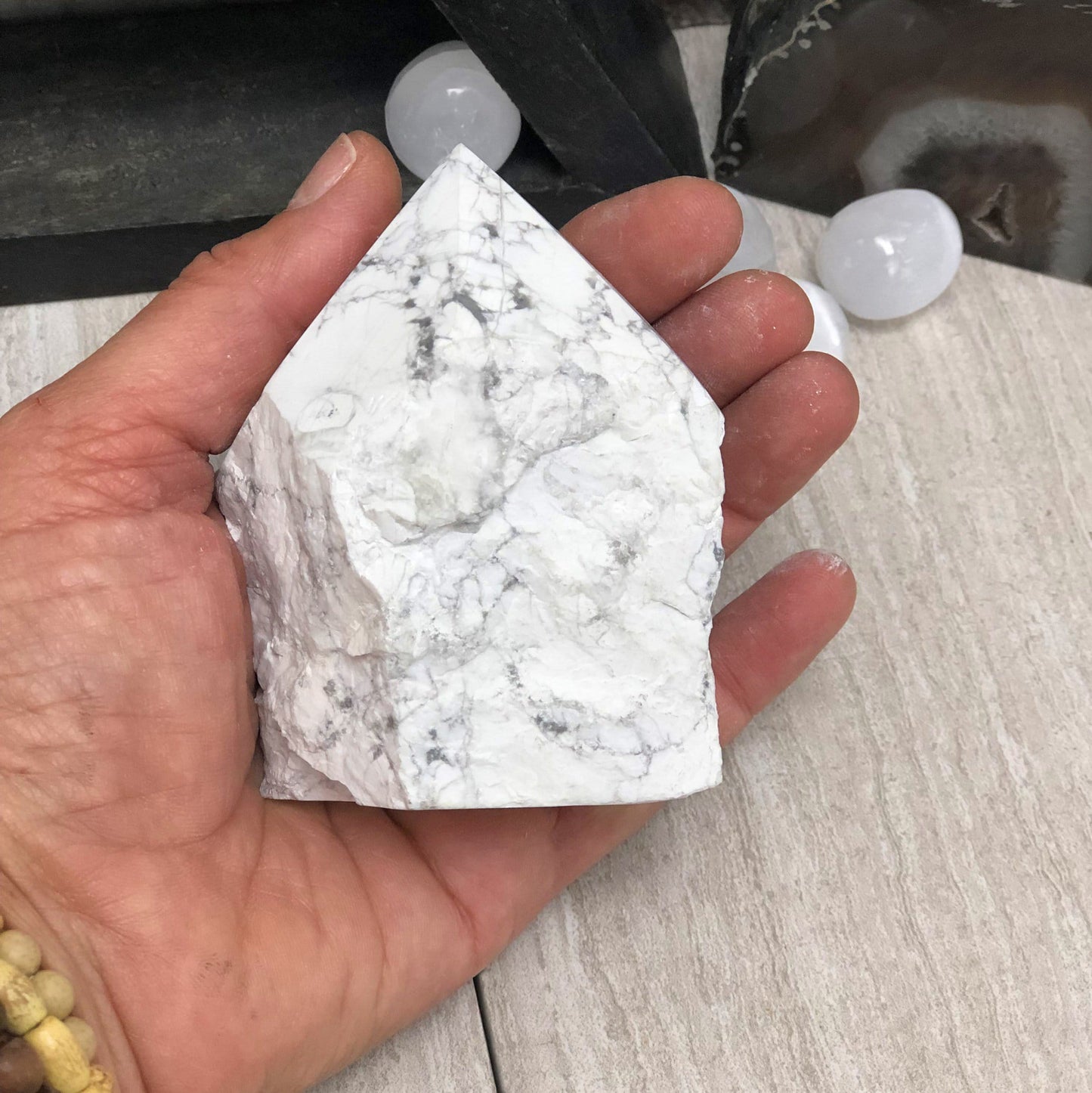 white howlite point with the top polished and the bottom left rough.  Held in a hand.