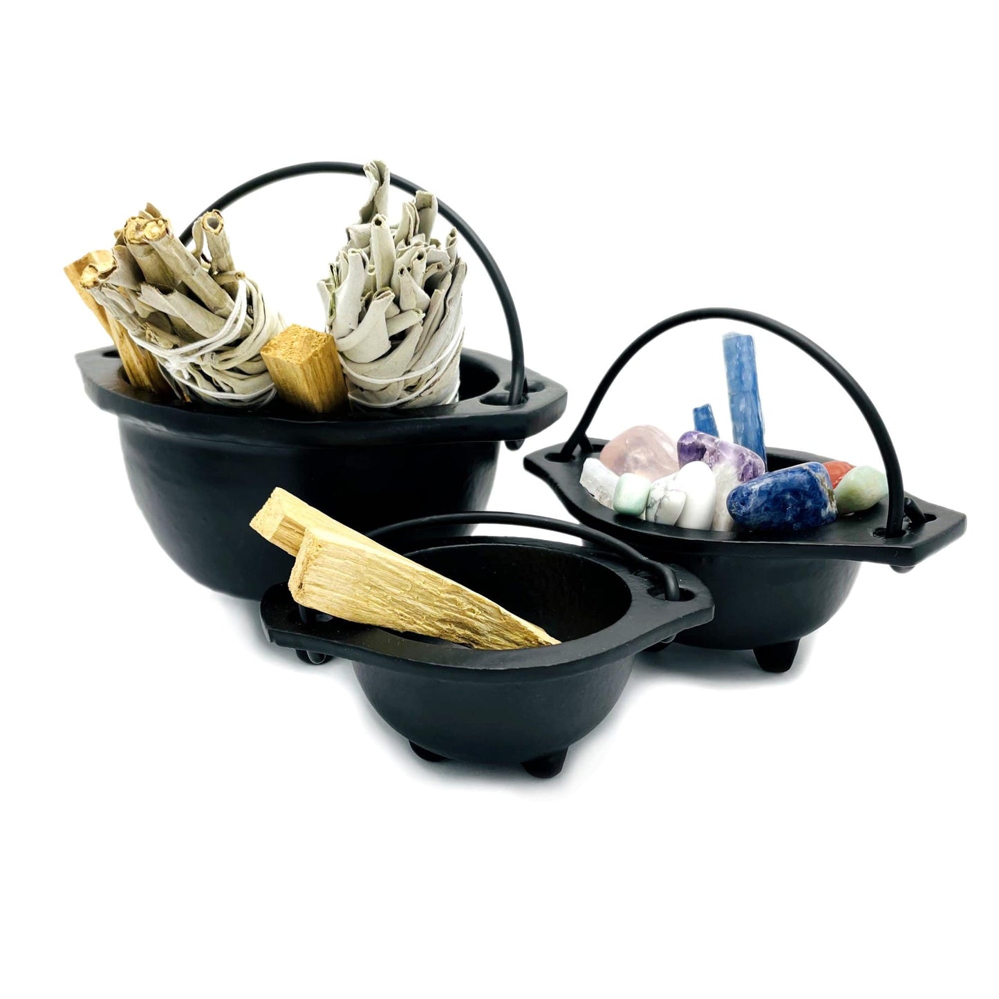 All three sizes of black iron cauldrons with sage palo santo or crystals inside them.