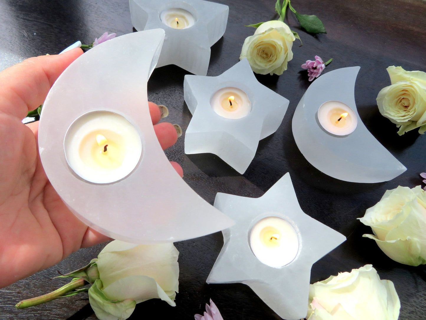 selenite crescent moon candle holder with candle (not included with purchase) in hand for size reference with other candle holders in background